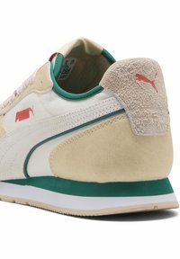 Puma sneakers featuring a beige and white upper, green accents, rubber sole, and textured suede on the heel. Red logo detail at the side.