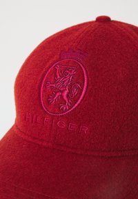Czerwona wełniana czapka z okrągłą koroną, z tonalnym haftowanym herbem lwa oraz logo "HILFIGER" z przodu. Teksturowane wykończenie.