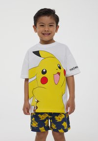 T-shirt bianco in cotone con una grande stampa gialla di Pikachu. Abbinato a pantaloni blu con un motivo ripetuto di Pikachu.