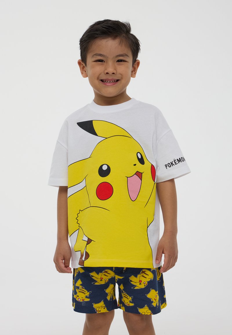 T-shirt bianco in cotone con una grande stampa gialla di Pikachu. Abbinato a pantaloni blu con un motivo ripetuto di Pikachu.