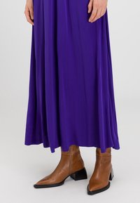 Lång lila klänning med ett svävande mönster, tillsammans med bruna läderankelboots med spetsig tå och kraftig svart klack.