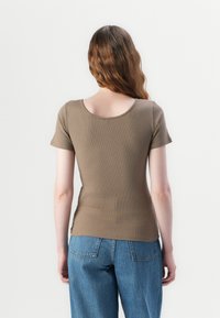 Haut marron à manches courtes côtelé avec un col rond, présentant un design ajusté. Associé à un jean en denim bleu ample.