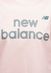 Απαλό ροζ ύφασμα με το λογότυπο "new balance" σε στυλιζαρισμένα μπλε γράμματα με ρίγες και μικρό λογότυπο New Balance στην πάνω δεξιά γωνία.