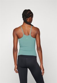 Camiseta sin mangas de Nike en color teal con tirantes delgados, diseño ajustado y textura suave. Combinada con leggins negros con detalles de costura.