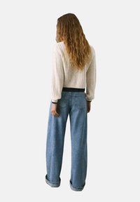 Maglione di filo a trecce crema con maniche a sbuffo, abbinato a jeans a gamba larga di colore blu chiaro, con orli arrotolati e tasche posteriori.