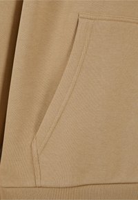 Beige genser med kengurulomme, ribbede mansjetter og kant. Myk stoff med en jevn tekstur og subtile sømdetaljer.