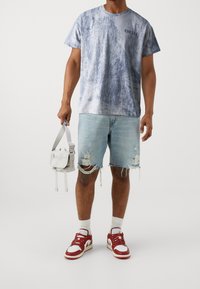 Světle modré tričko s batikováním, výstřih do crew neck, v kombinaci s poškozenými světle modrými džínovými šortkami. Doplňkem je malá bílá křížová taška. Červené a bílé tenisky.