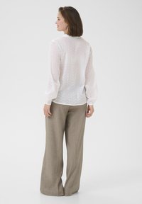 Witte, doorzichtige blouse met een subtiele patroontextuur, lange ballonmouwen, gecombineerd met beige wijde broekspijpen. Achteraanzicht getoond.