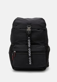 Zaino nero con patta superiore dotata di fibbia, tasca frontale con zip, tasche laterali in rete e tracolla con logo a marchio ripetuto.