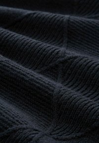 Close-up van donker gebreide stof met gestructureerde rib- en wafelpatronen, die zachte vouwen en fijne vezels laat zien.