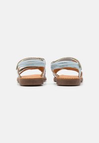 Bruna och blå sandaler med flera remmar och öppen häl. Sulan är platt med en strukturerad yta, tillverkad av läder och syntetiska material.