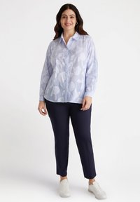 Camicia button-up azzurro chiaro a maniche lunghe con motivo floreale; abbinata a pantaloni navy e sneakers bianche. Vestibilità rilassata e tessuto strutturato.