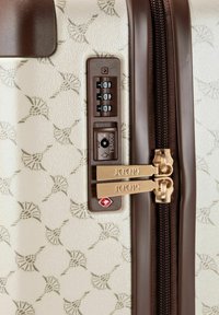 Walizka z twardą skorupą w kolorze kremowym z beżowym dekoracyjnym wzorem, wyposażona w brązowy zamek błyskawiczny i mechanizm zamykający, złote elementy oraz zamek TSA.