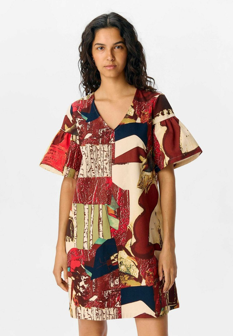 Robe à manches courtes avec un décolleté en V, présentant une variété de motifs abstraits dans des tons rouges, beiges et bleus sur un tissu léger.