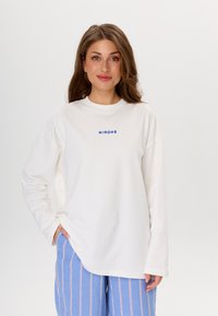 Chemise blanche à manches longues avec un graphique bleu "MIRONS" sur la poitrine, offrant une coupe décontractée et une texture de tissu douce.