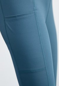 Høyt midjer leggings i en dyp blå nyanse. Laget av glatt, elastisk stoff; har sidelommer og forsterkede sømdetaljer.