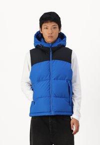 Gilet isolant bleu avec un panneau supérieur noir, une capuche et une fermeture éclair. Comprend des poches avant et une texture matelassée.