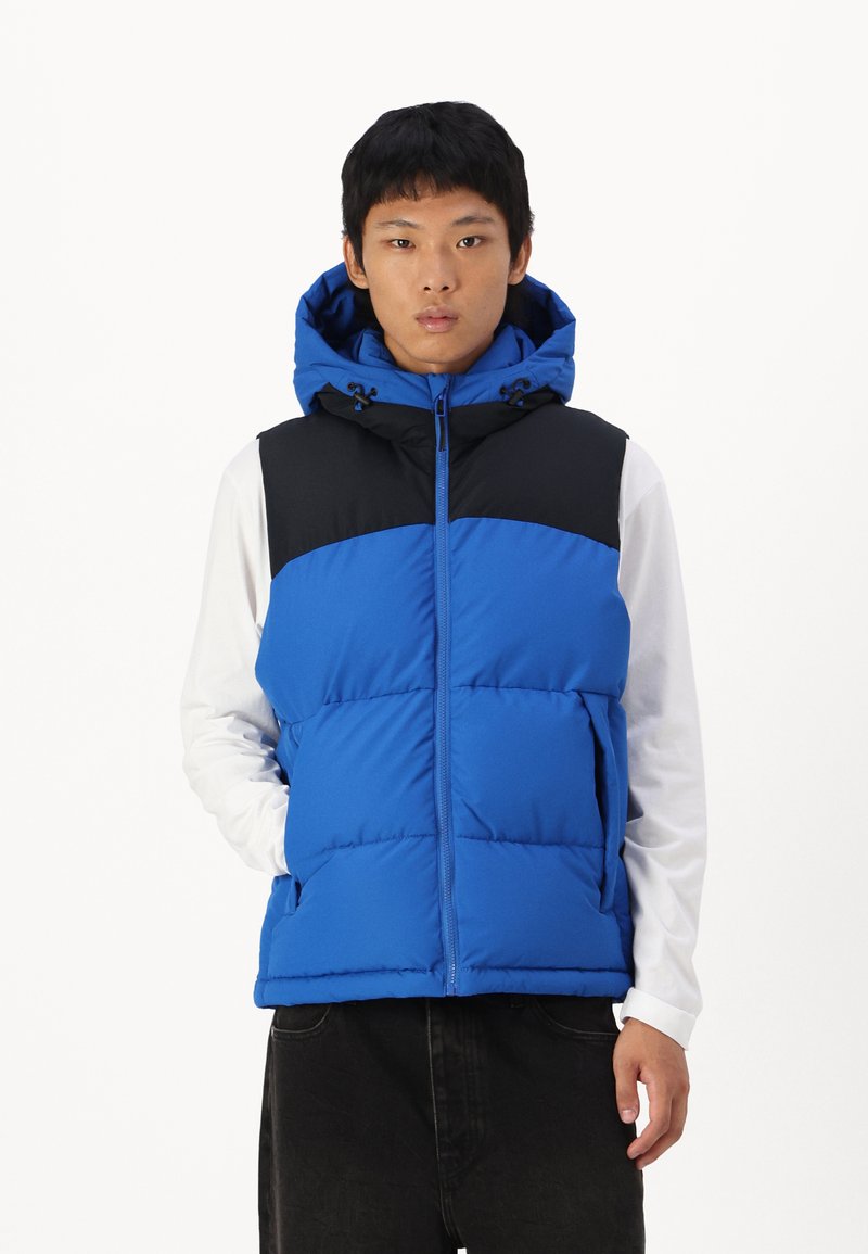 Gilet isolant bleu avec un panneau supérieur noir, une capuche et une fermeture éclair. Comprend des poches avant et une texture matelassée.