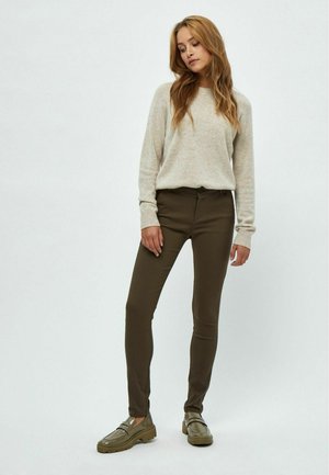 Pull beige à manches longues, associé à un pantalon ajusté vert olive et des chaussures slip-on vertes. Tricot simple et texturé avec une coupe soignée.