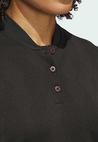 Polo nero con superficie strutturata, caratterizzato da un motivo sottile, colletto e tre bottoni bordeaux sulla parte anteriore.