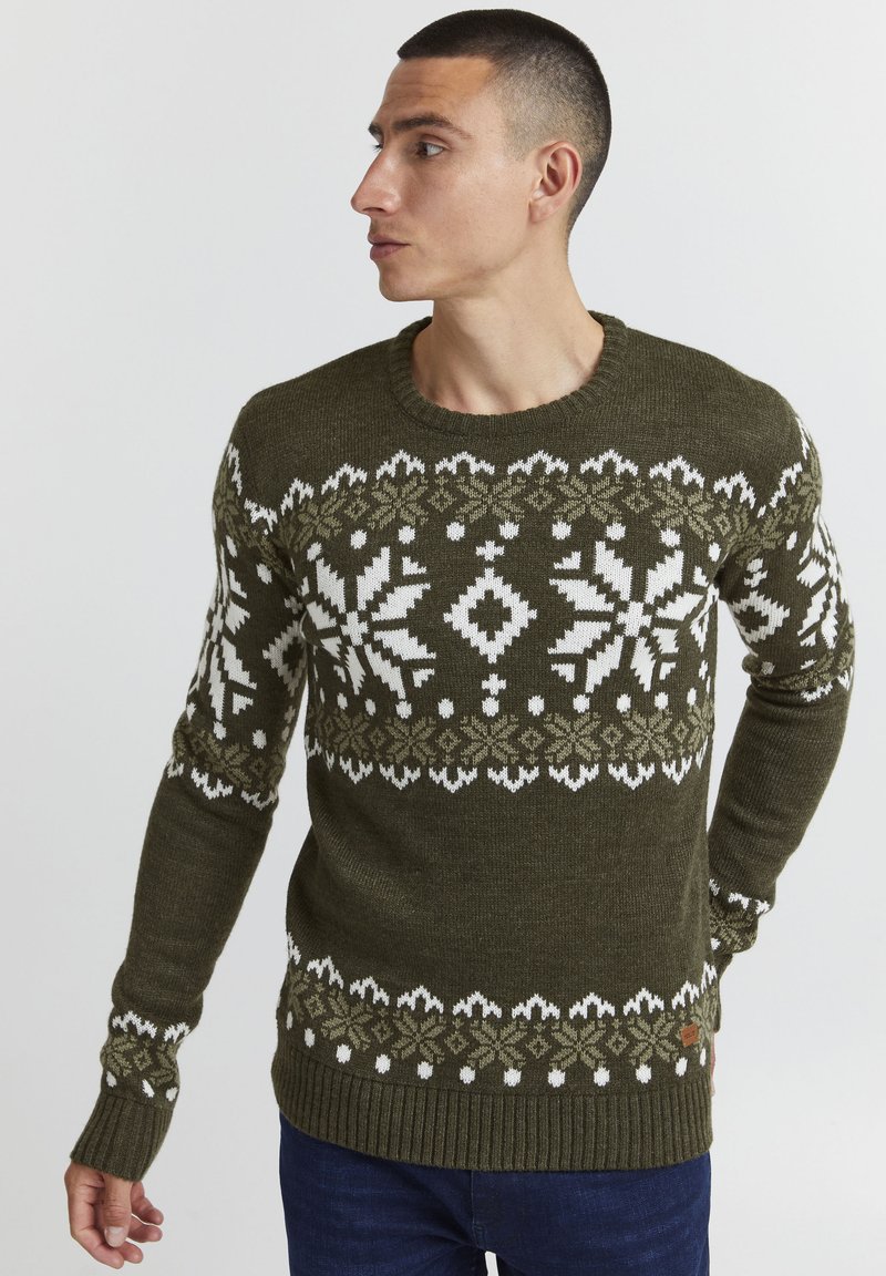 Pull en maille de couleur vert olive avec des motifs de flocons de neige et géométriques blancs, des poignets et un bas côtelés, un col rond, et une finition texturée.