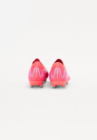 Red soccer cleats with a textured mesh upper, featuring a pink wave pattern, small turquoise accents, and a low-profile collar.