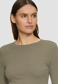 Olijfgroene geribbelde longsleeve top met een ronde halslijn, voorzien van subtiele stikdetails en een aangesloten silhouet.