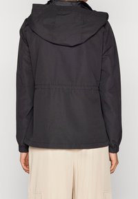 Giacca impermeabile nera con cappuccio, polsini elasticizzati e vita regolabile, caratterizzata da una texture liscia e un design minimalista.