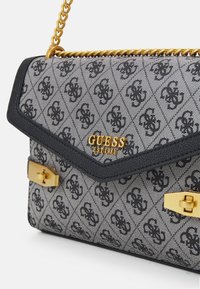 Czarna i szara torebka wzorzysta z klapą, złotymi akcentami metalowymi i łańcuszkowym paskiem. Wyróżnia się centralnym detalem z logo.