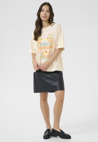 Grietos spalvos per didelės t-shirt su spalvinga grafika "Skleisk gerumą". Dėvima su prigludusia juoda odine sijonu ir juodais loafers. Slydus tekstūra.