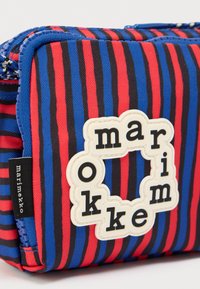 Μικρό τσαντάκι με φερμουάρ, με κάθετες ρίγες σε μπλε, κόκκινο και μαύρο χρώμα και λευκή κυκλική ετικέτα με το λογότυπο «marimekko».