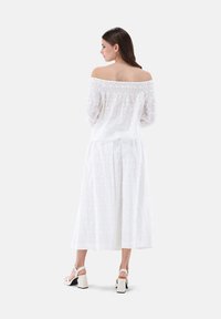 Weißes schulterfreies Kleid mit floraler Stickerei, langen Ärmeln und einem fließenden Rock. Kombiniert mit hellen, klobigen Absätzen.