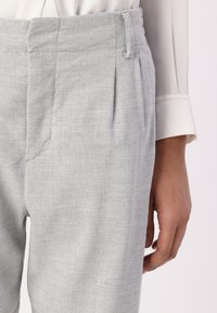 Pantalons en lin gris avec un tissu texturé, un design plissé et des poches en biais. Taille maintenue par des passants de ceinture.