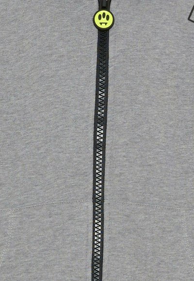 Felpa grigia con zip nera e cursore decorativo a forma di smile verde. Tessuto morbido senza motivi o loghi visibili.