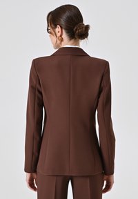 Bruine blazer met gestructureerd ontwerp, lange mouwen en notch revers. Gemaakt van gladde stof, met op maat gemaakte naden en een getailleerde silhoutte.
