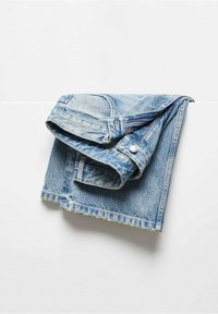 Chaqueta de mezclilla azul claro doblada sobre una superficie blanca, con costuras visibles, botones y detalles de dobladillo desgastado.