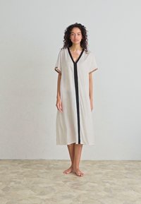 Lightweight beige dress with a black V-shaped neckline and front panel, short sleeves, and knee-length hem. Smooth fabric with minimal design.