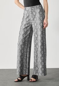 Wijdere broek in zwart-wit slangenprint, met een gladde textuur en gestikte taille. Gecombineerd met zwarte hakken.