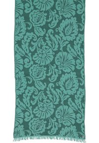 Tessuto rettangolare fiorato in tonalità teal e verde scuro, con bordi frangiati e un piccolo emblema circolare in un angolo.