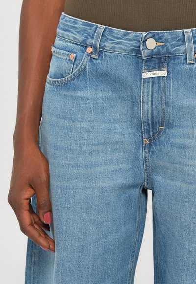 Light blue denim jeans feature a high waist, five-pocket design, and contrast stitching. Includes a button and zip closure, with label visible.