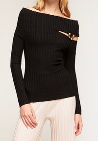 Black ribbed long-sleeve top featuring an off-the-shoulder design, a slit on one side, and a decorative hardware accent.