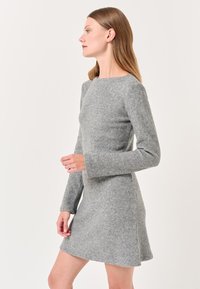 Robe en tricot gris à manches longues, avec un col rond, des fentes latérales et un corsage ajusté, mettant en valeur un tissu doux et texturé.