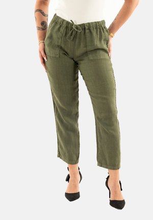 Pantalons en lin verts avec une taille élastique et un cordon de serrage, dotés de deux poches avant et d'une coupe fuselée. Portés avec des escarpins noirs.