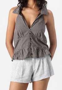 Hnědý a bílý kostkovaný bezrukávový top s volánkovým lemem, spárovaný se světle šedými pruhovanými šortkami. Lehký materiál a volný střih.