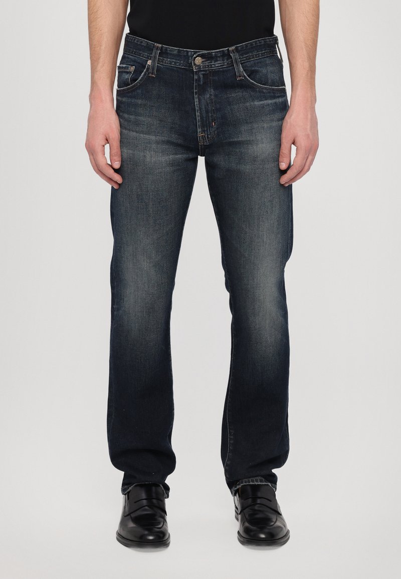 Tumedat sinised denim teksad sirge jala disainiga, millel on ees taskud, lukk ja õrn pleekimine. Kanda mustade kingadega.