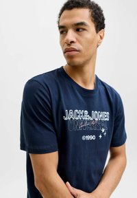 Una camiseta de algodón azul marino con mangas cortas, cuello redondo y un logotipo gráfico central en blanco y rosa con estrellas.