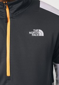 Sudadera negra con media cremallera y tela texturizada, cremallera naranja y logotipo blanco en el pecho. Incluye un acento gris claro en el hombro.