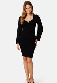 Černé šaty s dlouhými nabíranými rukávy, obepnutým pasem a výstřihem do V. Hladký materiál a délka ke kolenům. Ž�ádné viditelné vzory ani akcenty.