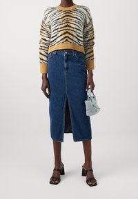Pull en tricot avec des rayures tigre jaunes, noires et crème ; jupe midi en denim bleu avec une fente à l'avant ; sandales à talons noires ; sac à main bleu clair.