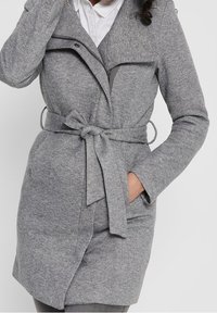Cappotto in misto lana grigio con chiusura a zip e colletto a scialle. Presenta una vita con cintura e tasche laterali, con una finitura morbida e texturizzata.